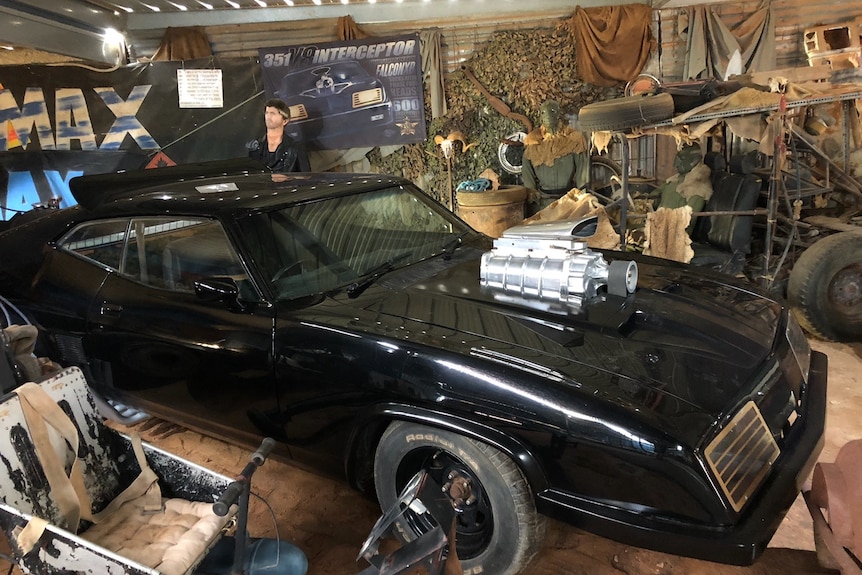 A black two-door car surrounded by Mad Max memorabilia.