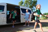Children exit a mini-van at a primary school, as bus driver Deb holds open door