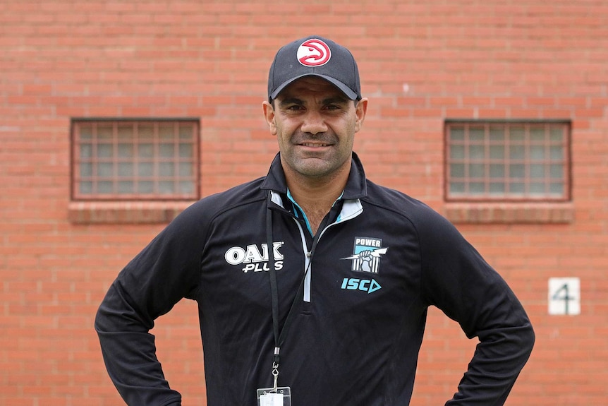 Lindsay Thomas wearing Port Adelaide gear in front of a red brick wall in the Port Lincoln prison