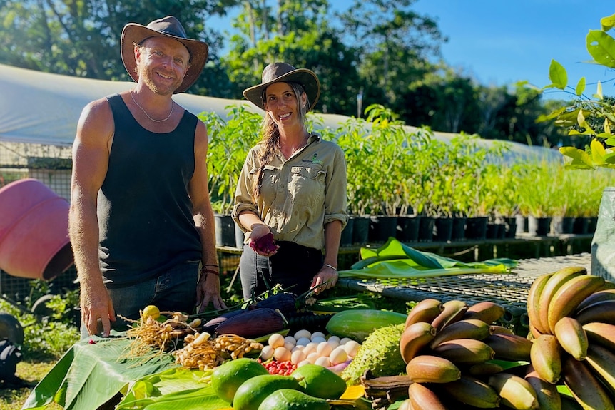 A photo of a man and a woman standing next to a table of fruit and vegetables at a farm.