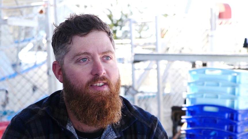 Tyson Pollard sitting in front of plastic crates and traps for catching octopus.