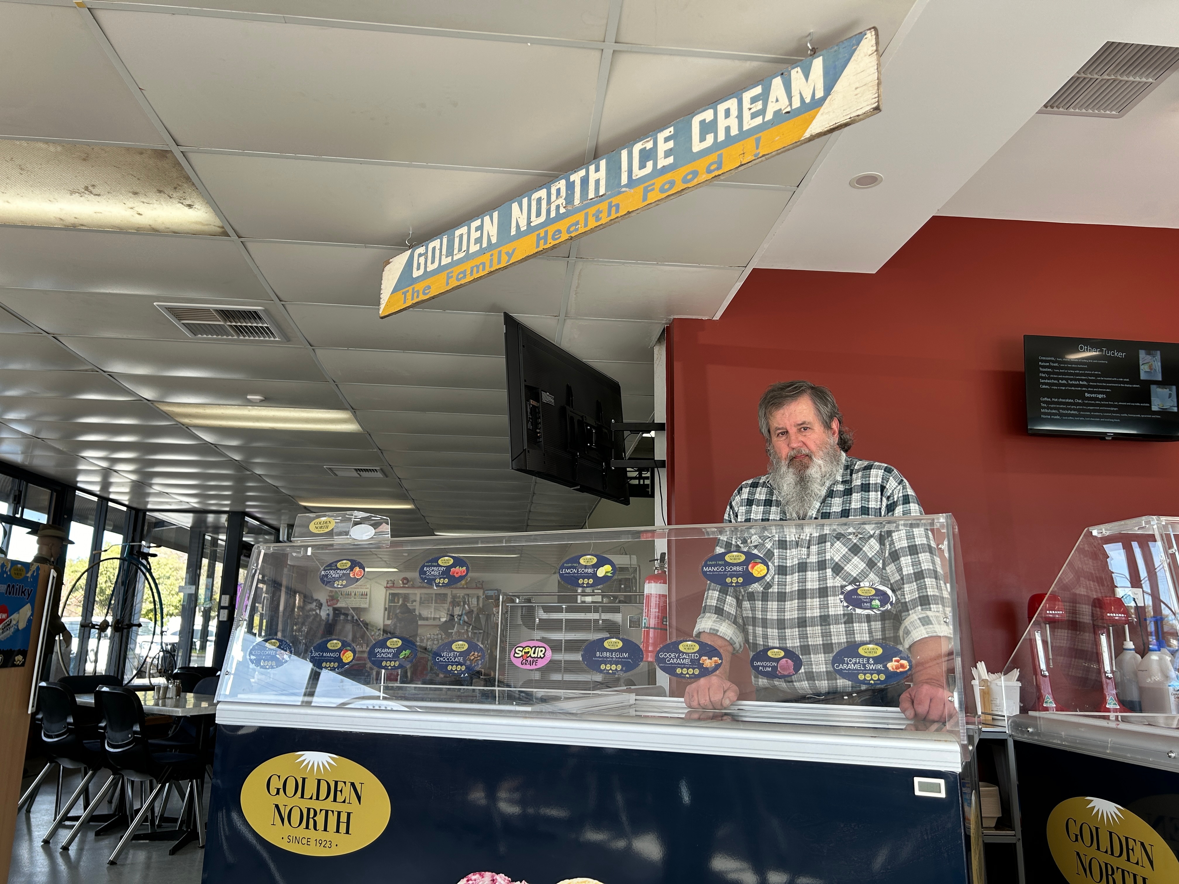 Un hombre de pie detrás de una barra de helado. 