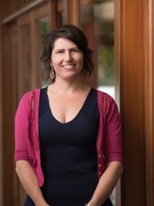 Samantha Crompvoets, with brown hair, standing wearing a blue dress and pink cardigan, smiling.