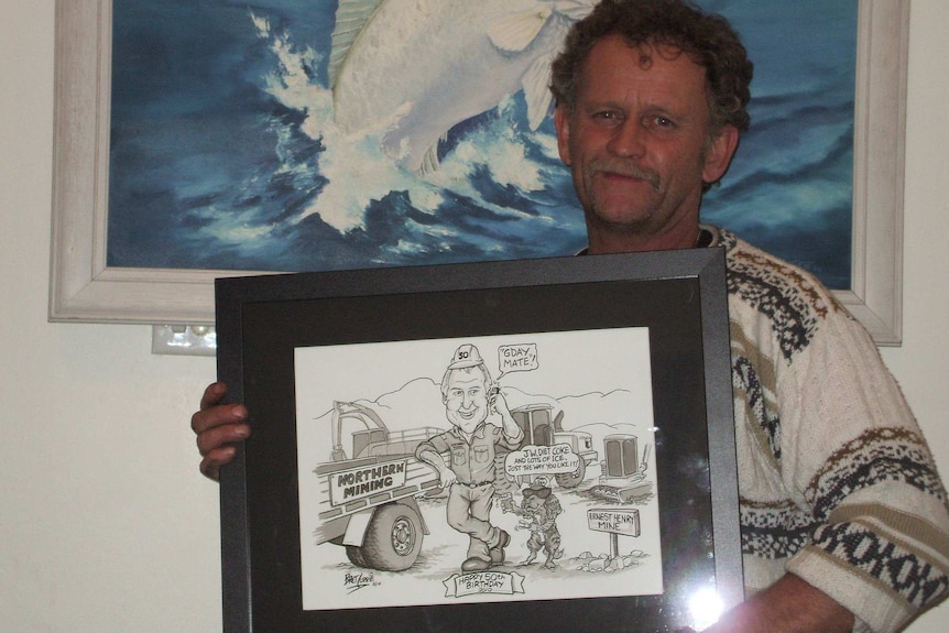 A photo of a man holding a framed cartoon.