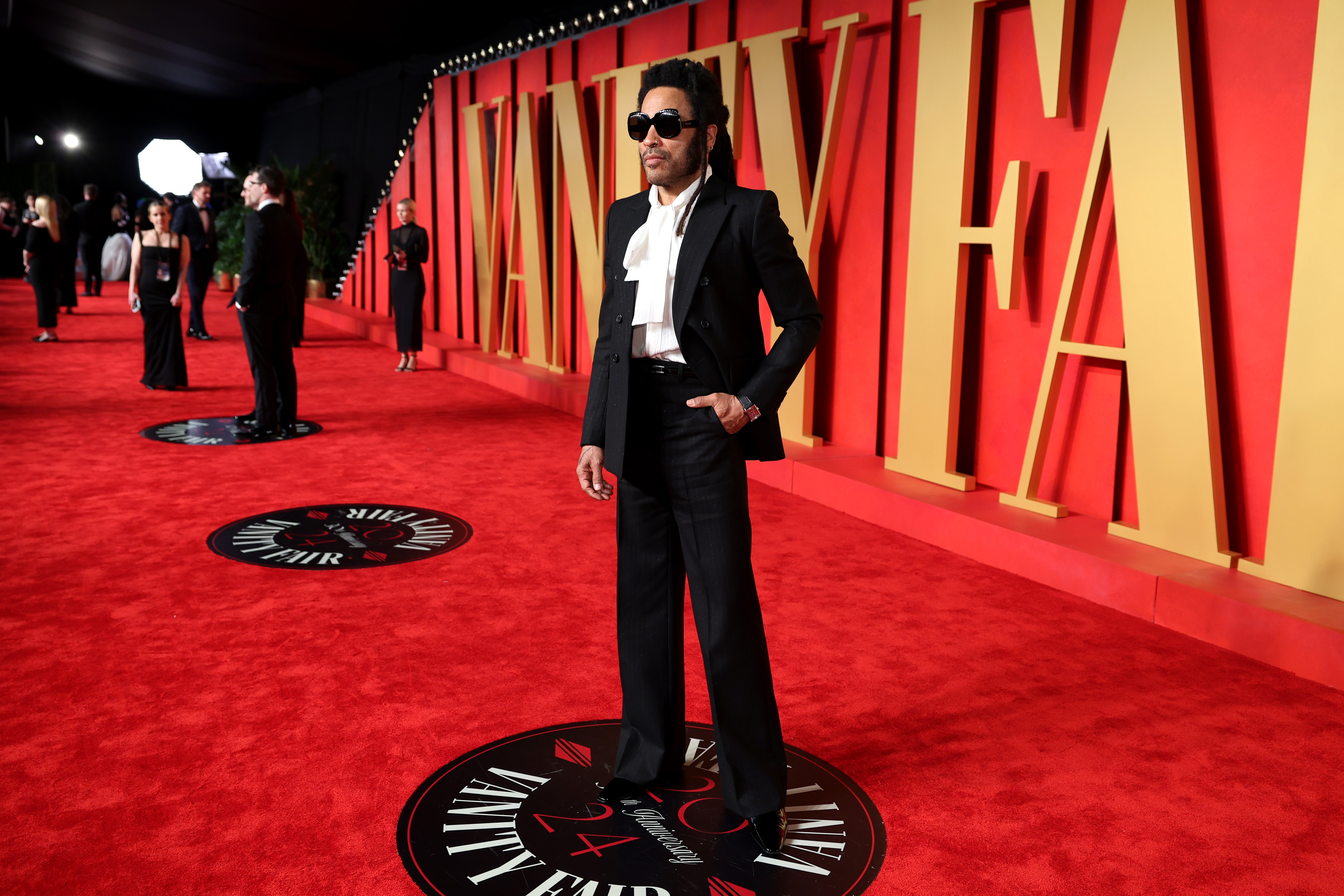 Lenny Kravitz in a black and white suit on a red carpet. 