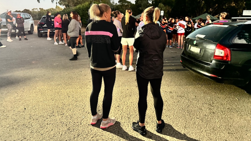 Two women with back to camera facing crowd of runners at running event