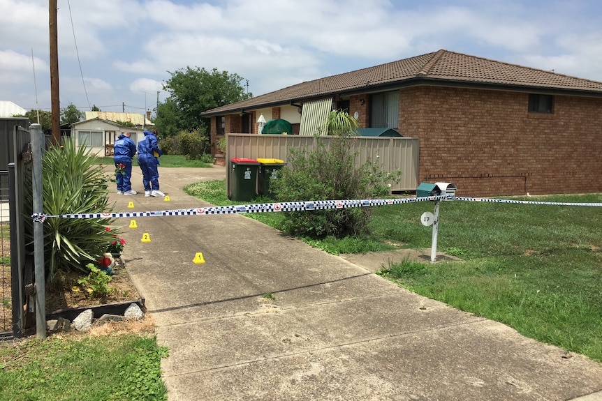 A brick unit surrounded by police tape with forensic police placing yellow marker