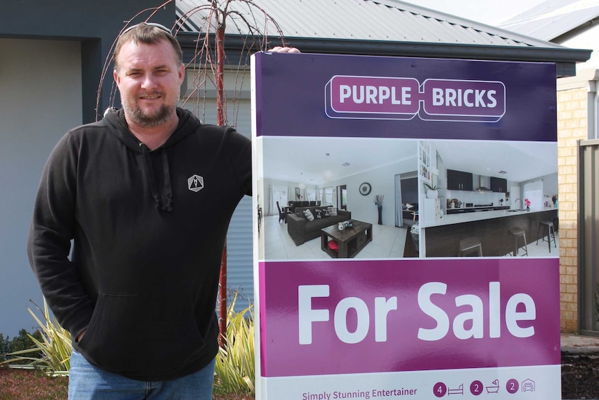 Andrew Hayden standing next to a Purple Bricks for sale sign on the front lawn of his Byford home.