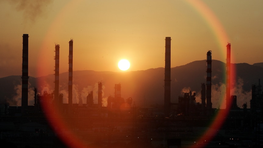 The sun sets over the chimneys of an oil refinery