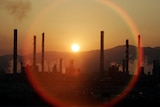 The sun sets over the chimneys of an oil refinery