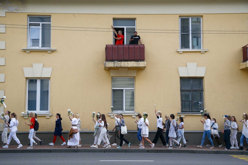 Two men look down from a balcony as women rally in solidarity with protesters injured in the latest rallies in Belarus.