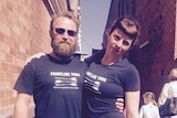 A man and a woman stand with their arms around each other's shoulders wearing black shirts that say Frontline Yoga