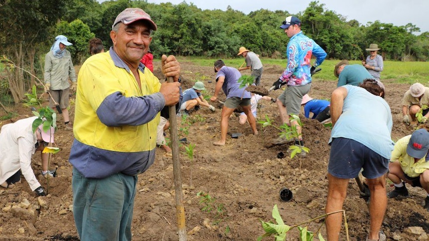 A farmer leans on his shovel surrounded by volunteers planting trees on a degraded section of his cane farm