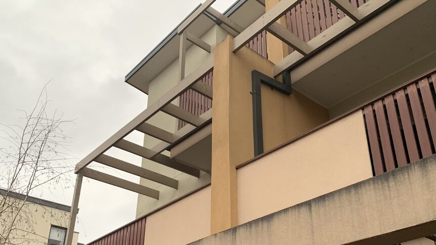 A photo of the exterior of the apartment complex shows a series of panels of cladding.