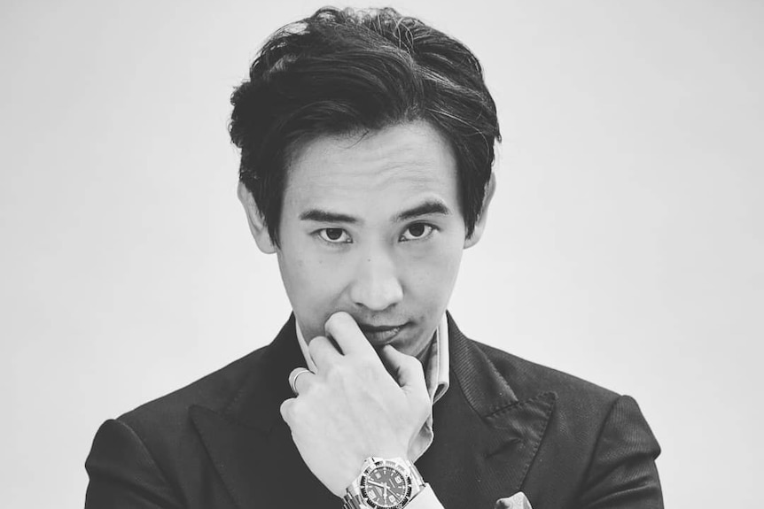 A handsome young man poses in a black and white photo with his hand on his chin