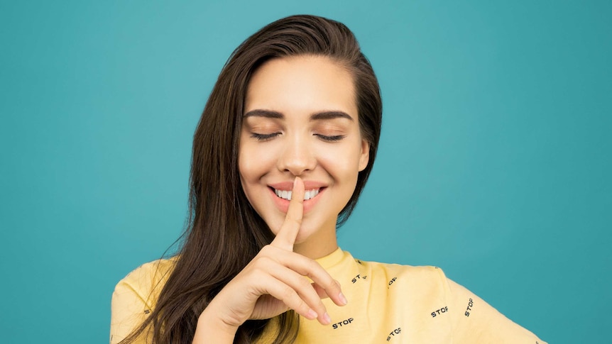 Woman holding finger to her mouth as if to say "shhhh" in a story about which types of secrets can cause harm in relationships.