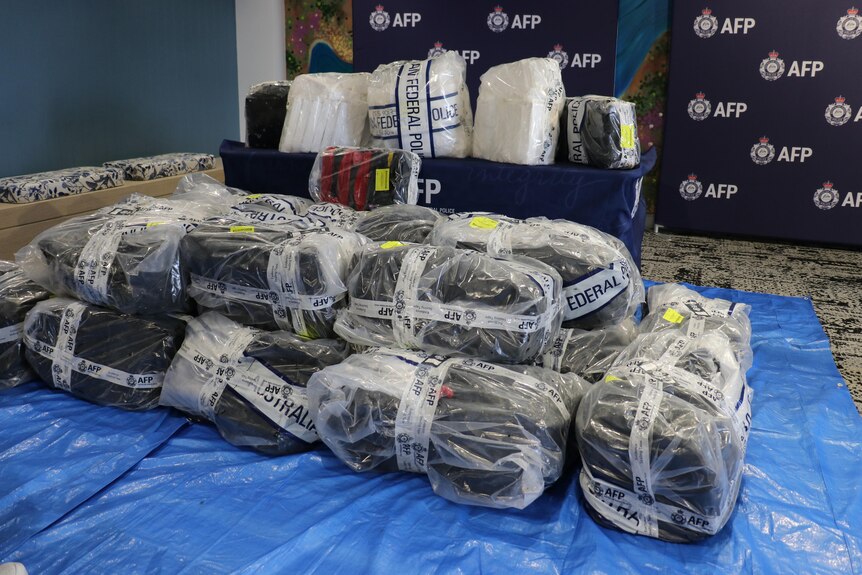 A wide shot of large plastic-wrapped packages containing cocaine, taped up with AFP tape, at a media conference.