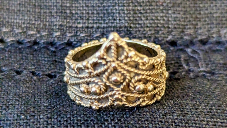 A gold wedding band with gold filigree and an point on one side.