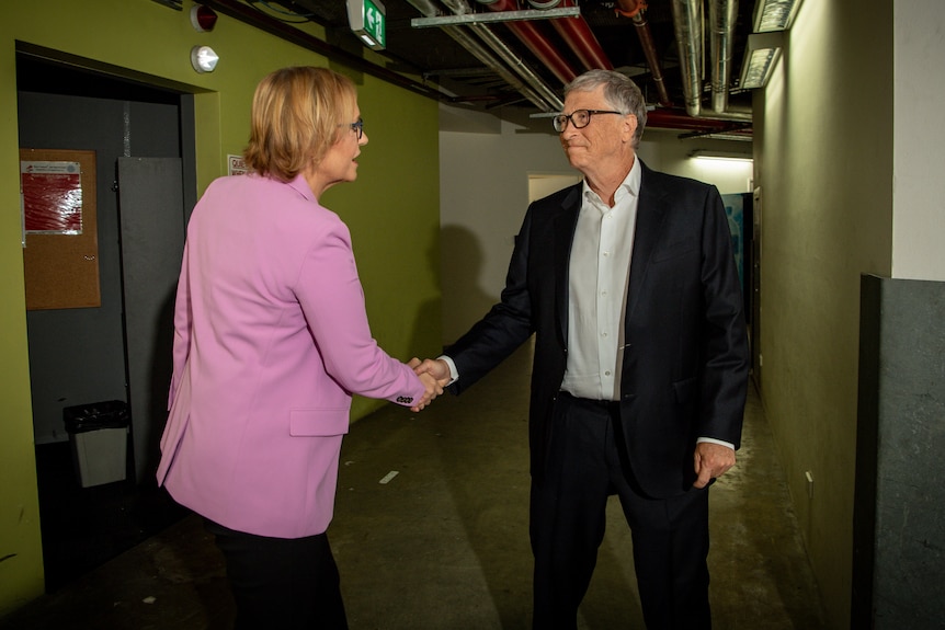 A woman and a man shake hands in a hallway.