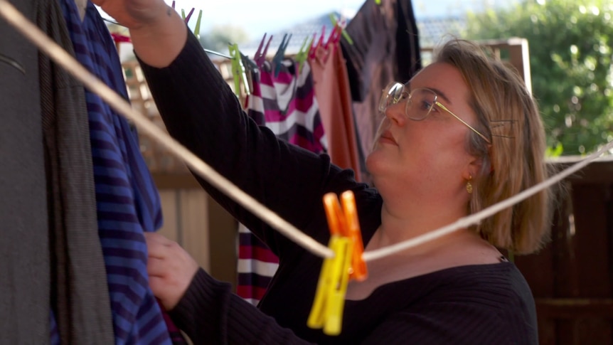 A woman with short blonde hair hangs laundry on a washing line