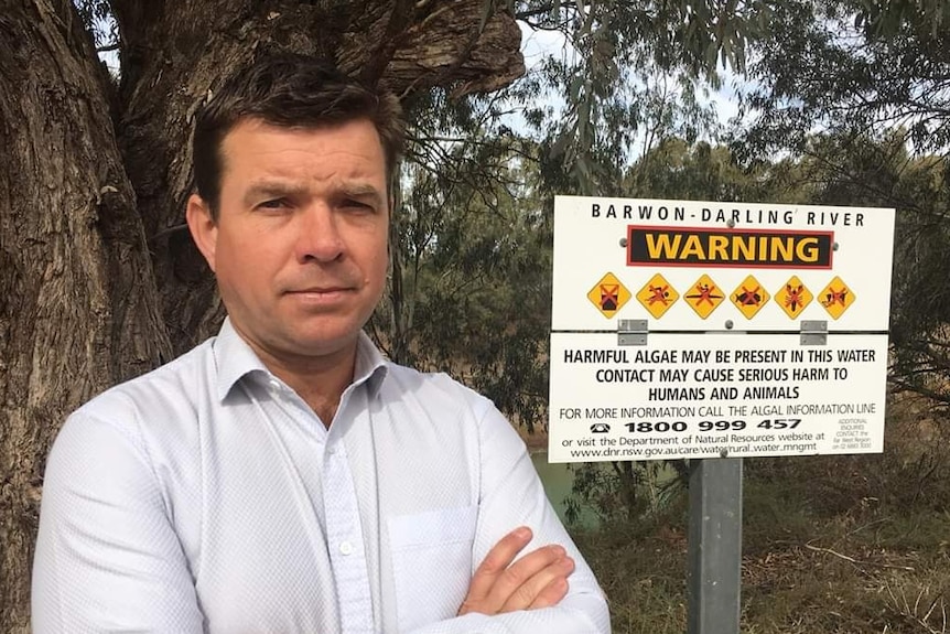 A man stands in front of a warning sign in the bush with his arms crossed.