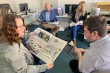 Staff sitting in chairs in a circle reading copies of a newspaper