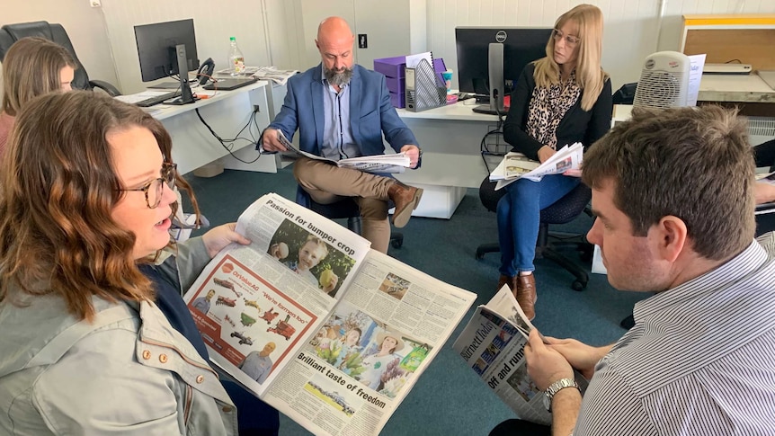 Staff sitting in chairs in a circle reading copies of a newspaper