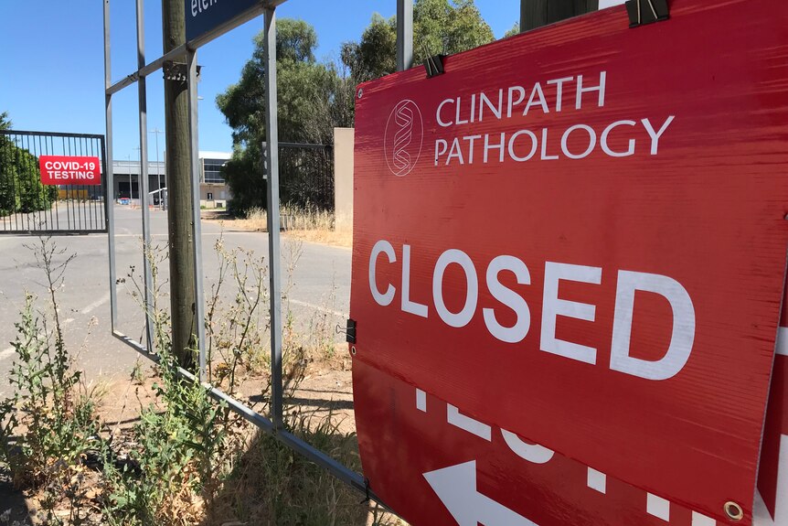 A red sign that reads 'closed' is stuck on a gate outside a COVID-19 testing facility