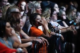 A woman tears up and puts her hand to her face at a concert barricade
