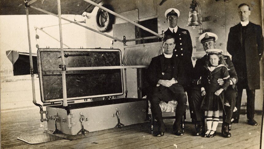 Nancy Bentley sits with four men, two wear naval caps. She is dressed in a naval uniform and cap herself.