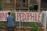 TV still of man hanging pedophile sign on fence outside Dennis Ferguson's unit in Sydney