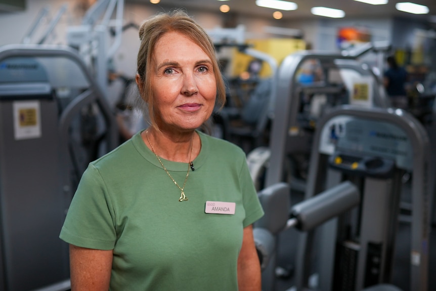 Woman with strawberry blonde hair and green t-shirt smiles in gym.