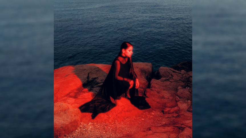 Artwork for Sofia Kourtsis' 2023 album Madres showing her in red and blue tones, squatting cliffside overlooking the water