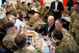 Joe Biden holds up a slice of pizza while eating lunch with US troops.