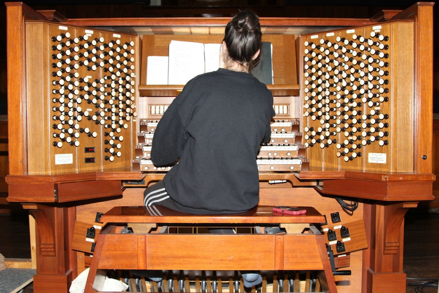 A woman sits at the portable organ console which controls the four-story high grand organ at Melbourne Town Hall.