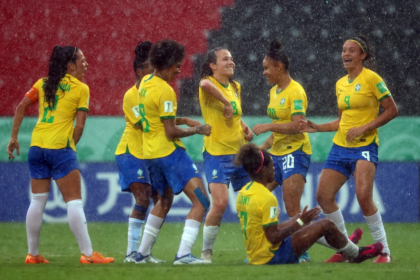 A female soccer team wearing yellow and blue dance in the rain