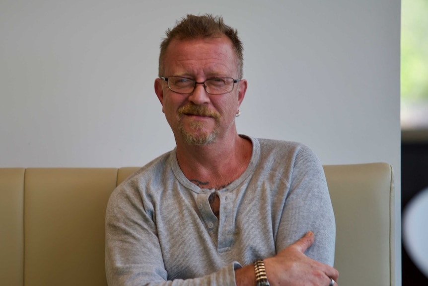 Andrew Hodson sits on a couch with his arms folded, wearing a half smirk.