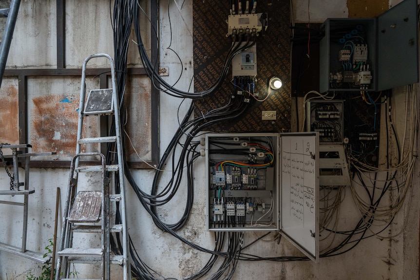 An open fuse box on a wall near a ladder 