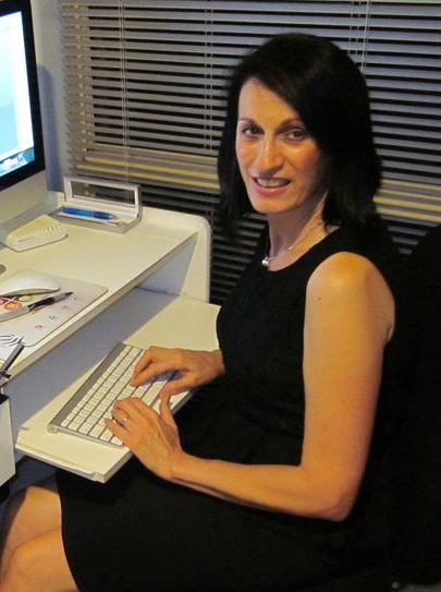 A woman sitting at a computer, about to type and looking at the camera.