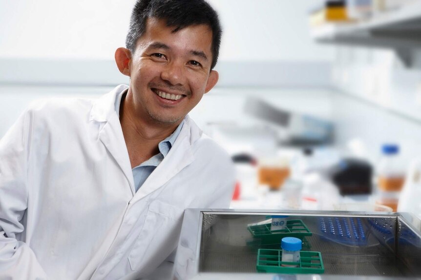 Associate Professor Tri Phan, dark hair and tanned skin smiles in a clinical laboratory, wear a white coat.