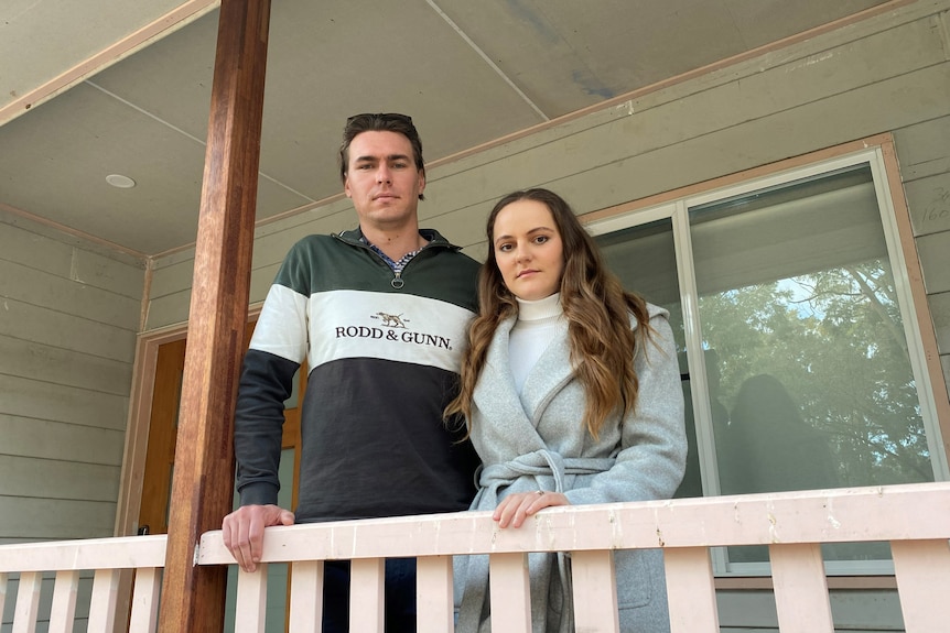 Young couple stand together looking concerned on their verandah.