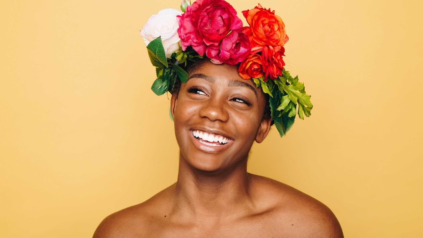 Closeup of woman smiling wearing flower crown with a bright yellow backdrop to represent simple skincare routines