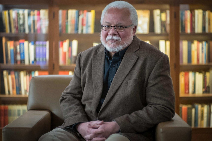 A middle aged African American man poses in front of books.