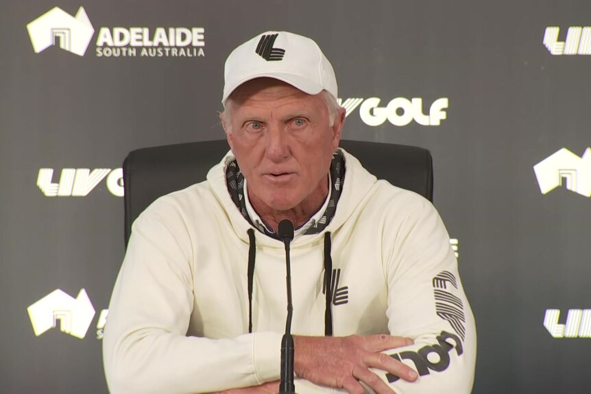 A man in a white hoodie and cap speaking at a press conference