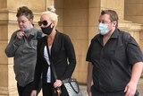 Three masked people walking outside a court building, one has his mask pulled down.