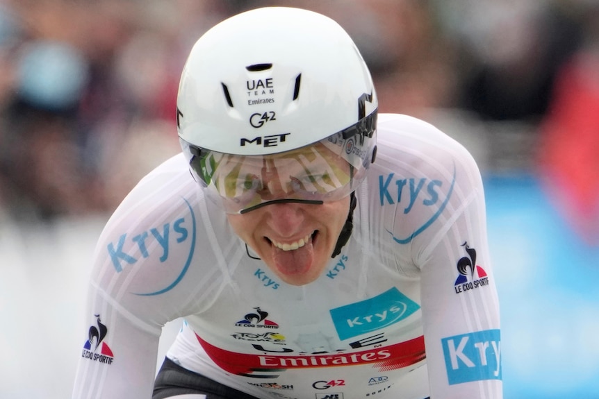 Tadej Pogacar sticks his tongue out while riding, wearing a white skin suit