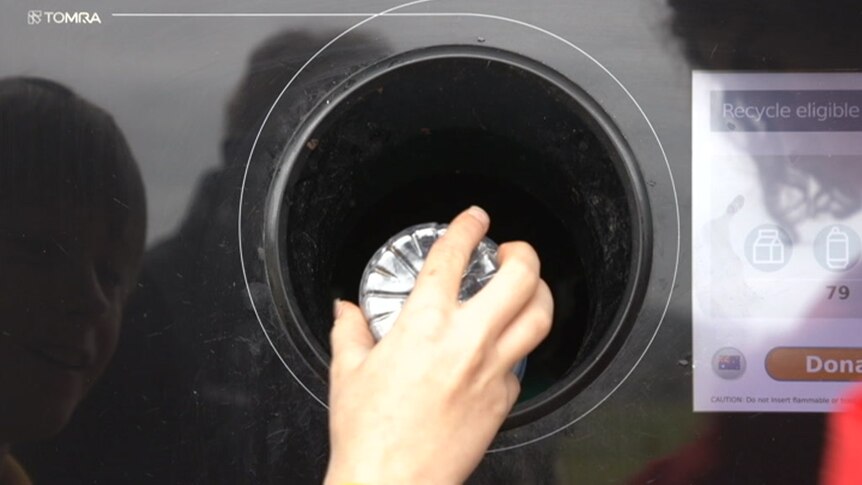 A hand places a plastic bottle into a NSW recycling machine.