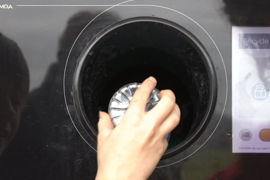 A hand places a plastic bottle into a NSW recycling machine.