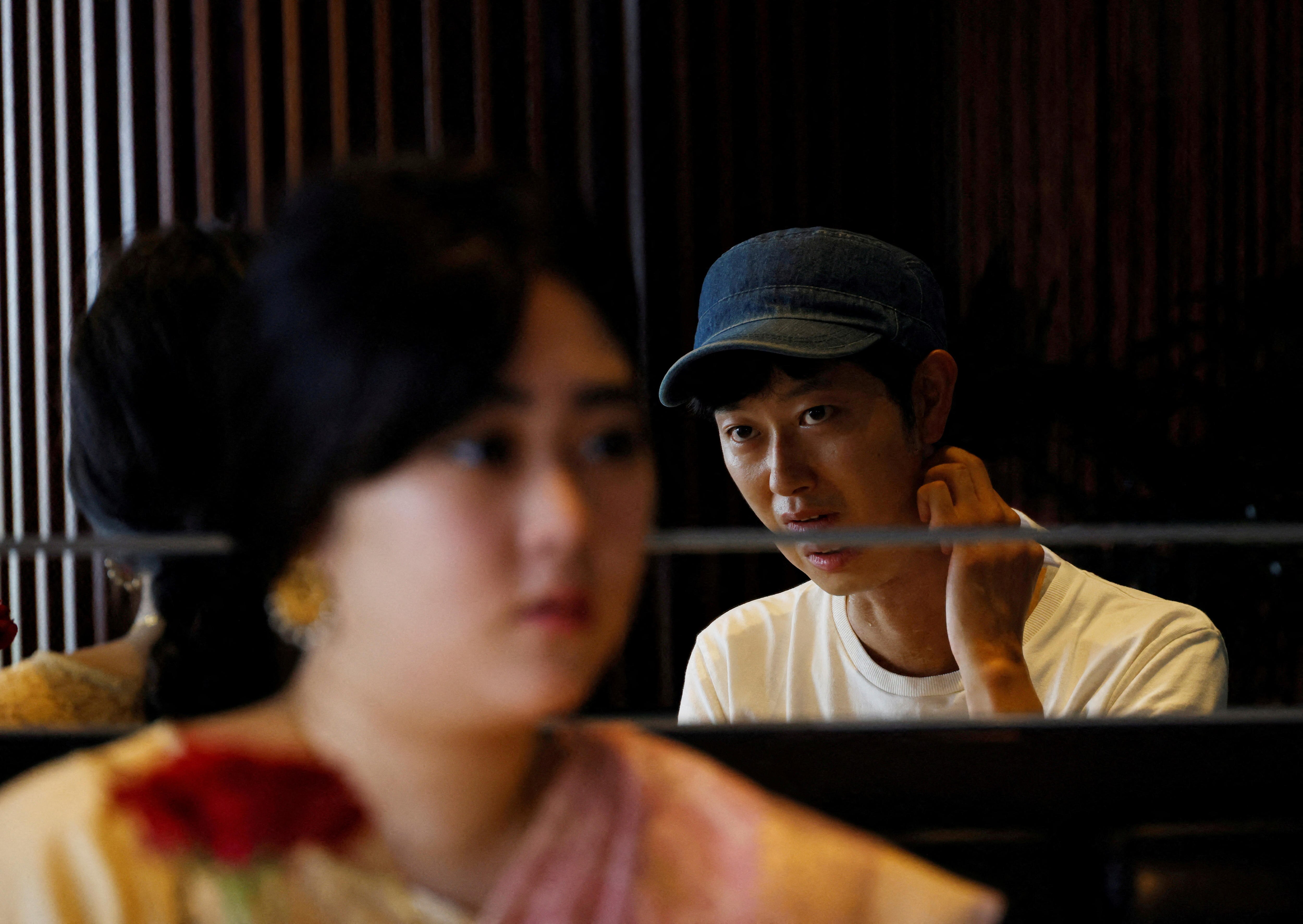 A young Japanese man is reflected in a mirror while talking to a young Japanese women in a sari. 