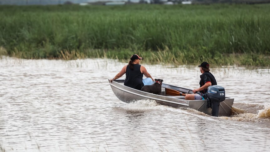 A pair drive a tinnie along a flooded section of the Pacific Highway